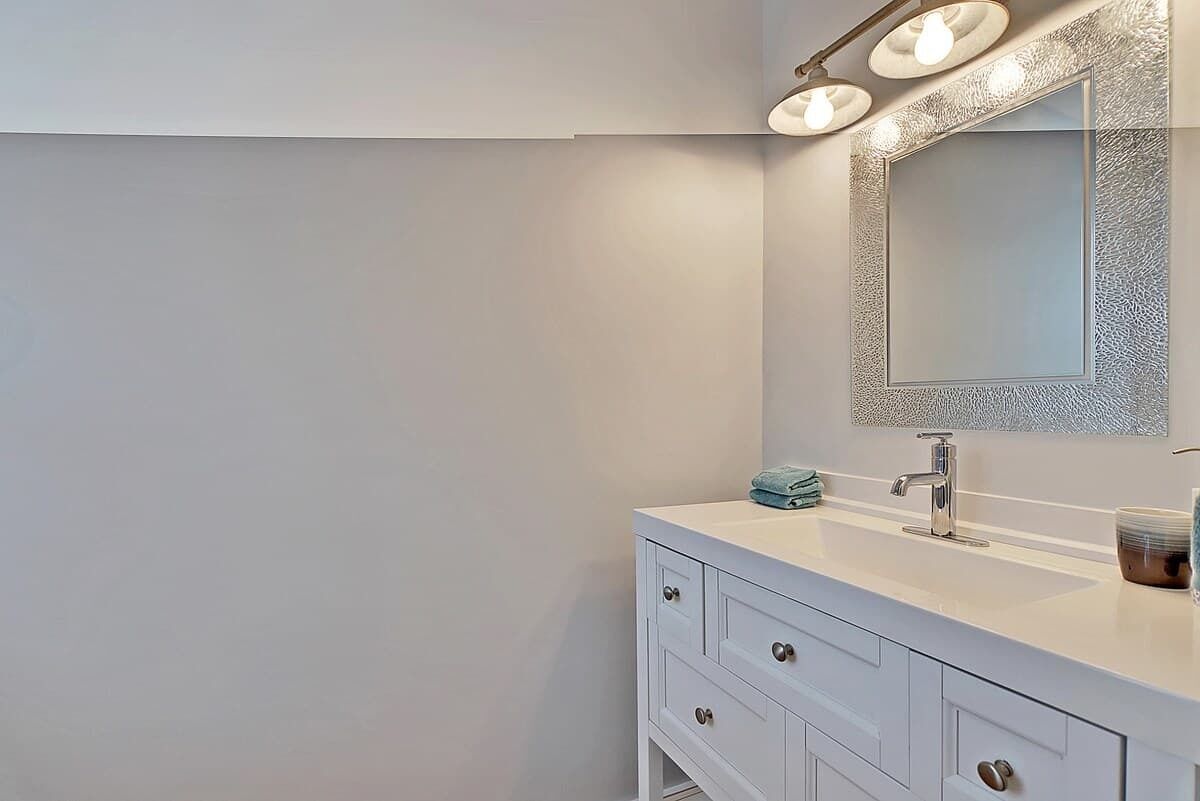 A modern bathroom with a white vanity, a large mirror with a textured frame, and three wall-mounted lights.