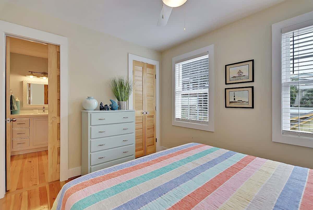 A bedroom with a bed, dresser, closet, and windows.