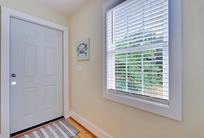 A hallway with a white door, a window with blinds, and a rug on the floor.
