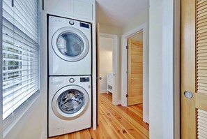 Une buanderie équipée de deux machines à laver superposées, avec un plancher en bois et une porte donnant sur une autre pièce.