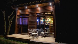 Une structure en bois comprenant un bar, des portes vitrées et une terrasse avec des chaises.