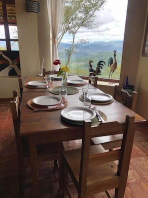 A dining table set with plates, glasses, and a vase with flowers, overlooking a scenic view with mountains and a bird statue.
