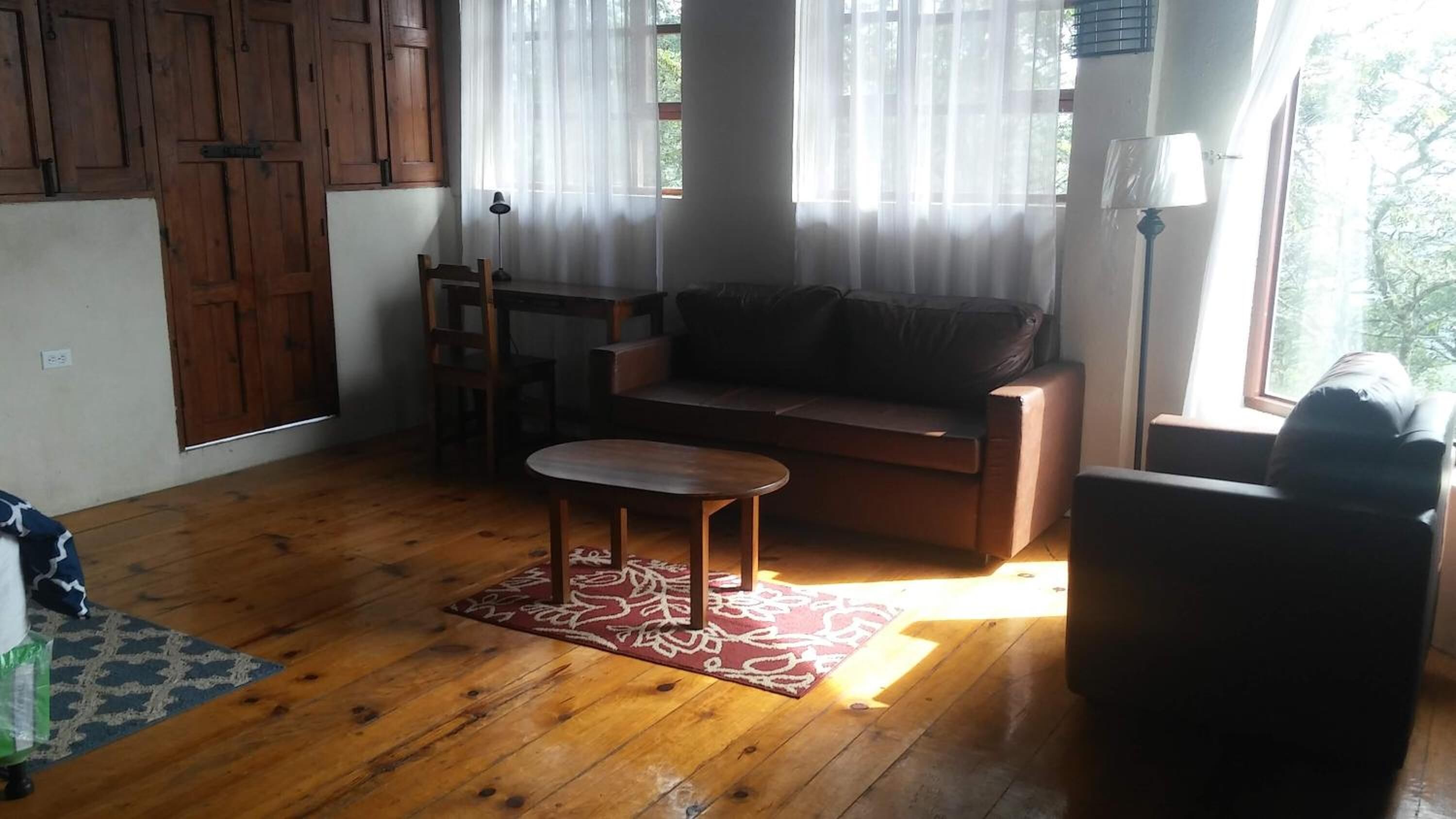A living room with wooden flooring, a sofa, a small table, and a lamp.