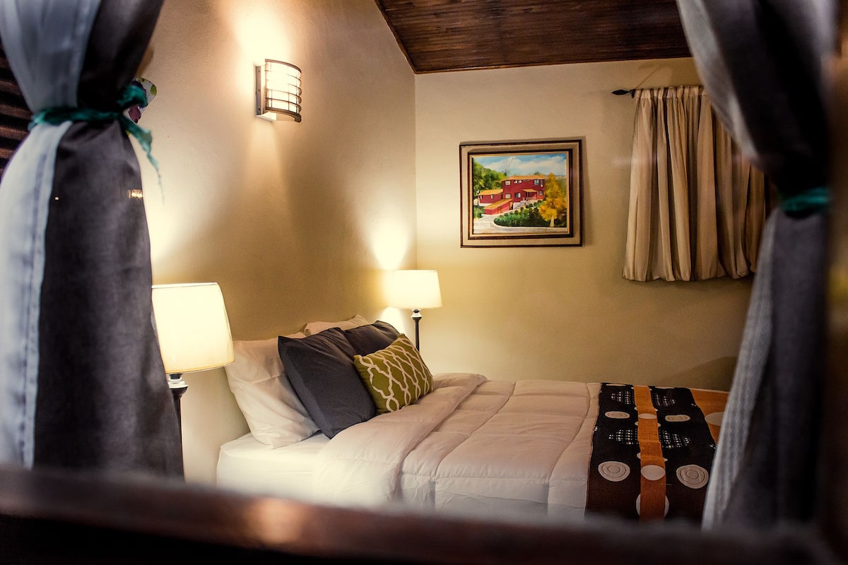 A hotel room with a bed, two bedside lamps, a framed picture on the wall, and curtains.