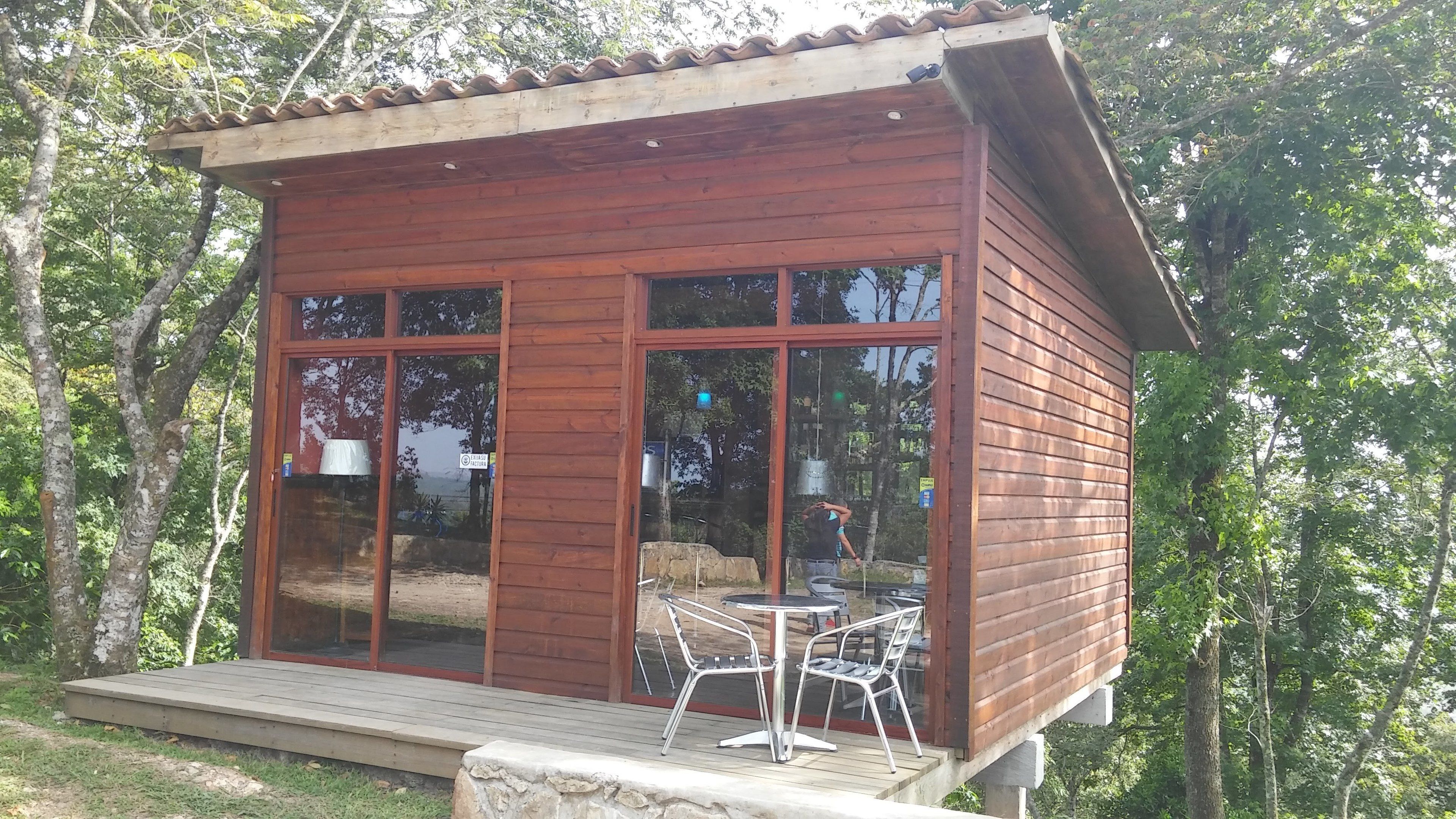 A wooden cabin with large windows, a deck, and outdoor seating.