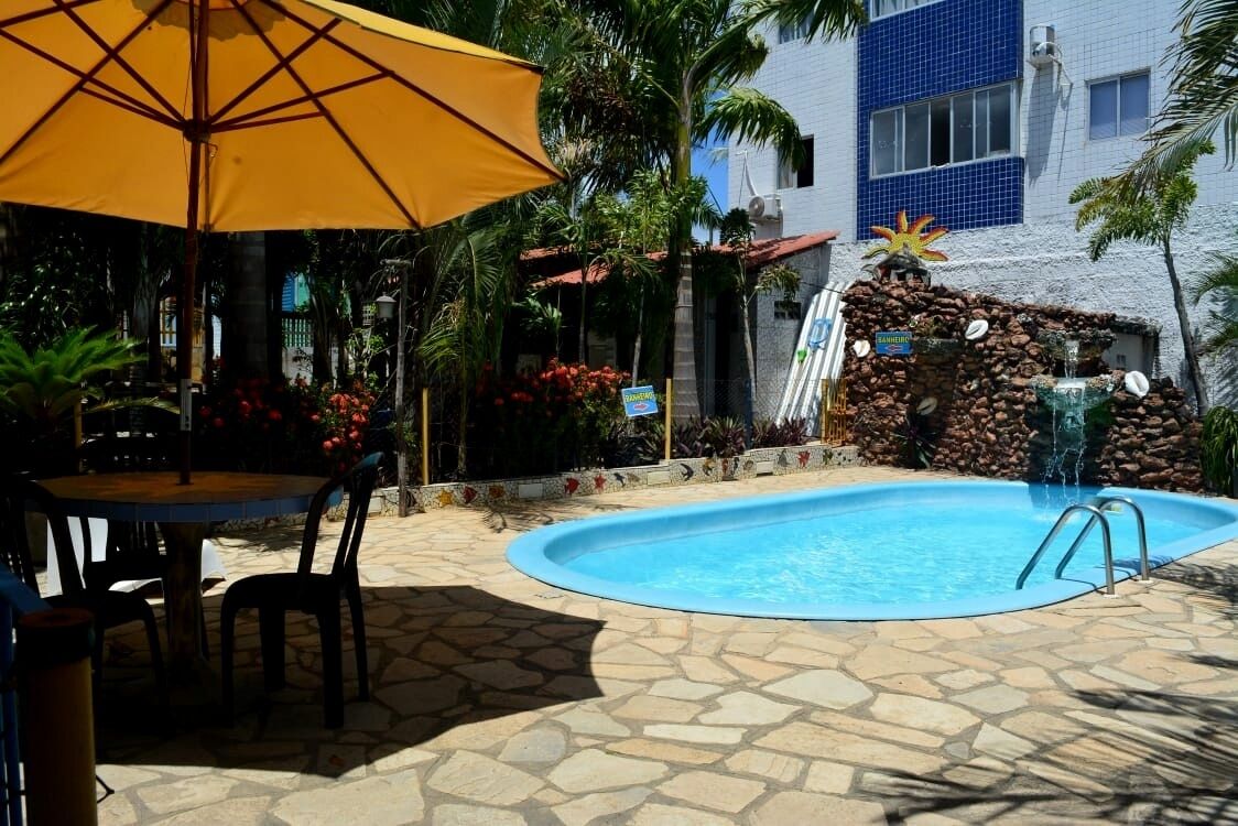 A swimming pool with a stone patio, a yellow umbrella, and a small waterfall feature.
