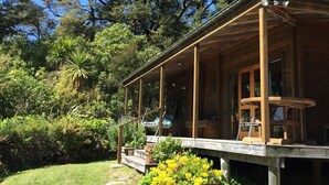 A wooden cabin with a porch, surrounded by lush greenery and trees. - Heart of Kaiteriteri: Absolute Privacy nestled between both beaches  (Kaiteriteri)