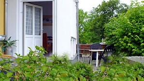 Una casa amb façana blanca, una porta i una finestra. Hi ha una taula i caires a l'exterior.