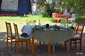An outdoor dining area with a round table covered by a tablecloth, surrounded by chairs.