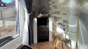A living room with a fireplace, a glass coffee table, and a view of the outside. - Cozy apartment, Cuxhaven-Döse (Cuxhaven)