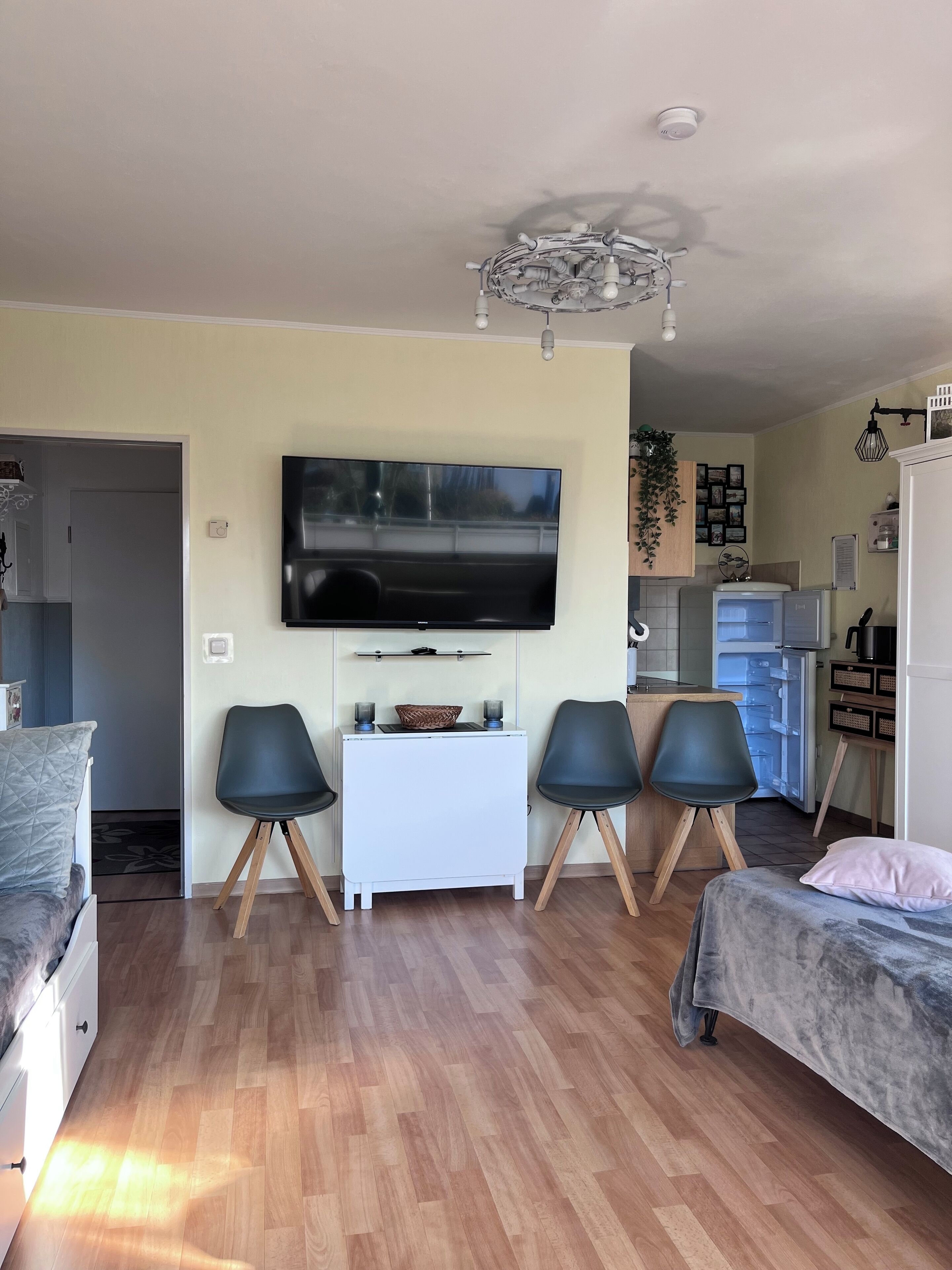 A modern living room with a flat-screen TV, two black chairs, a white coffee table, and a bed with a pink pillow.
