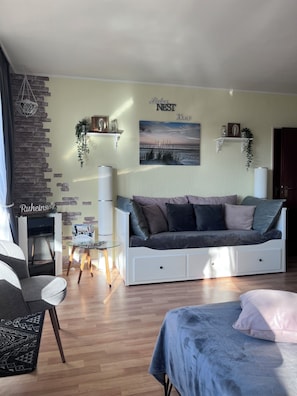 A modern living room with a sofa, a glass coffee table, a fireplace, and a wall-mounted shelf with decorative items. - Cozy apartment, Cuxhaven-Döse (Cuxhaven)