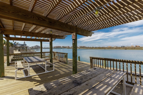A wooden deck with picnic tables and a railing overlooking a body of water.