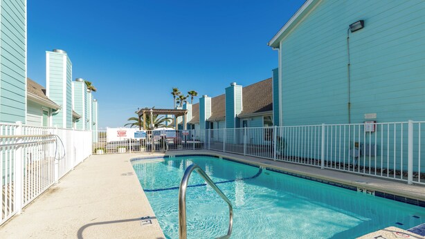 A swimming pool with a metal ladder, surrounded by a white fence, and adjacent to a building with a light blue exterior. - Waterfront Escape | Pet-Friendly & Beach Nearby (Corpus Christi)