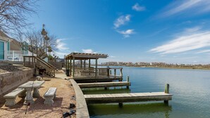 A waterfront dock with benches and a gazebo, a clear sky, and a distant view of buildings. - Waterfront Escape | Pet-Friendly & Beach Nearby (Corpus Christi)