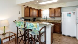 A kitchen with wooden cabinets, a white refrigerator, a microwave, and a coffee maker. There is a small table with a lamp and two bar stools with patterned cushions. - Waterfront Escape | Pet-Friendly & Beach Nearby (Corpus Christi)