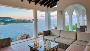 A spacious balcony with a view of the sea and a sunset. There is a wicker sofa and a glass table with candles and wine glasses. - Villa Amalia (Philipsburg)