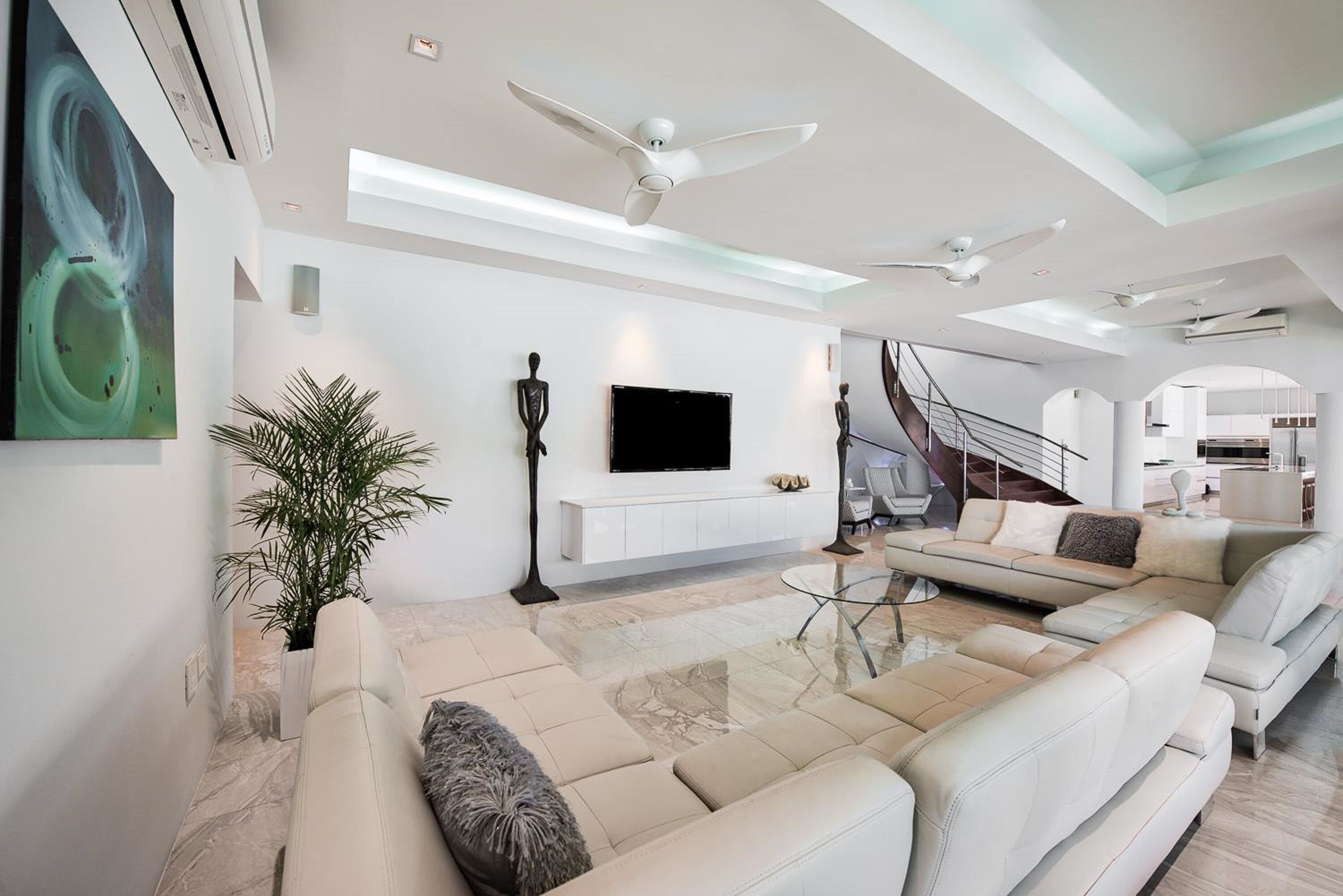 A modern living room with a large sofa, a flat-screen TV, and a staircase leading to an upper level.