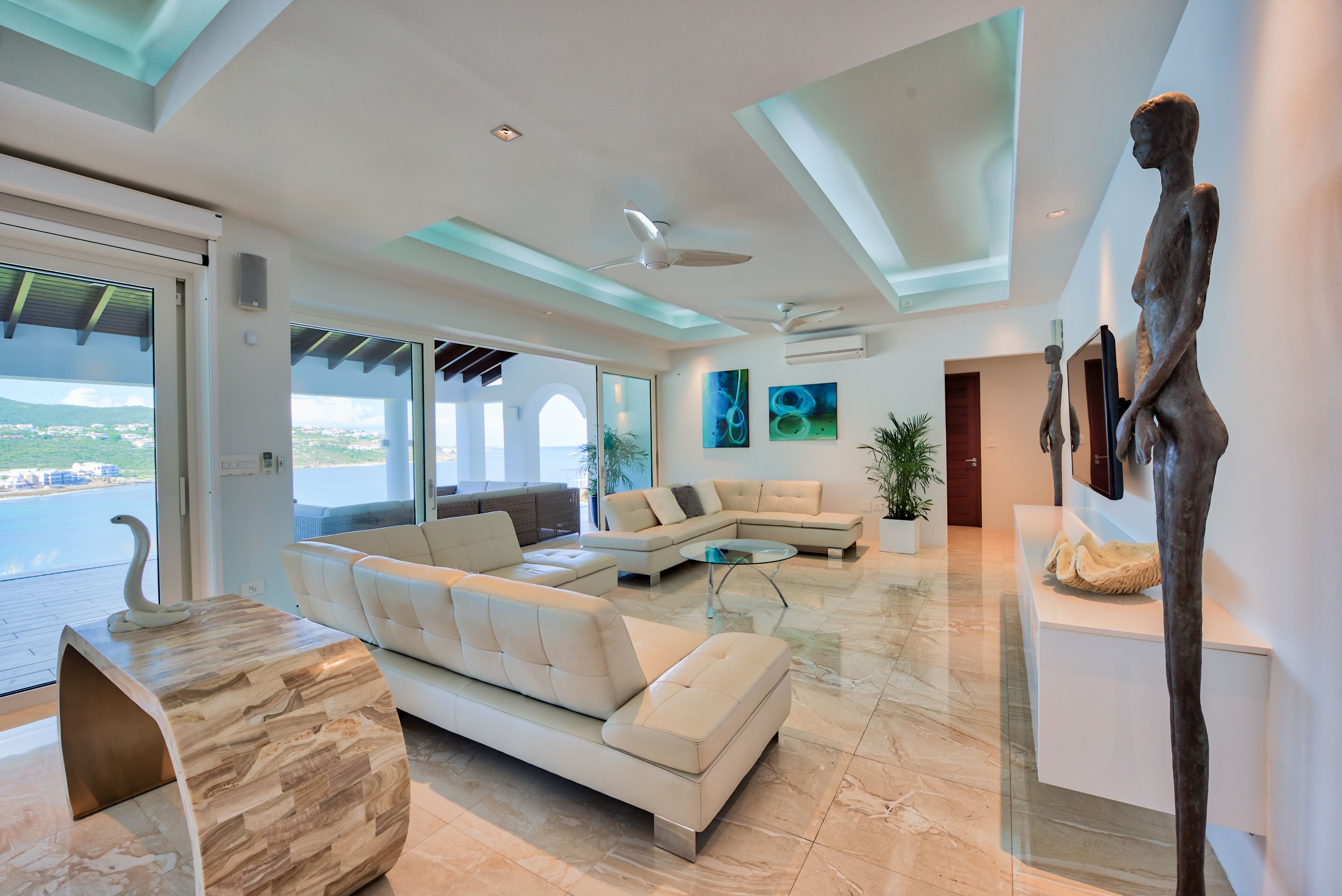 A modern living room with a curved white sofa, a glass coffee table, and a sculpture on a pedestal.
