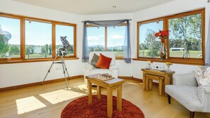 Quarto com um telescópio, um sofá branco, uma poltrona estampada e uma mesa de madeira.