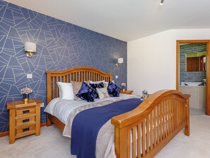 A bedroom with a geometric-patterned wall, a wooden bed frame, a bedside table with a lamp, and a bathroom visible through an open door. - 3 bedroom accommodation in Carrbridge, near Aviemore (Carrbridge, near Aviemore)