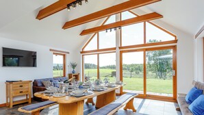 Cozinha espaçosa com uma grande mesa de jantar posta para seis pessoas, vigas de madeira e amplas janelas com vista para o exterior.