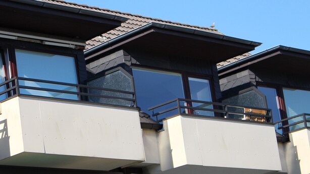 A building with multiple balconies, large windows, and a tiled roof.