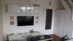 A modern living room with a flat-screen TV, white cabinets, and a staircase.