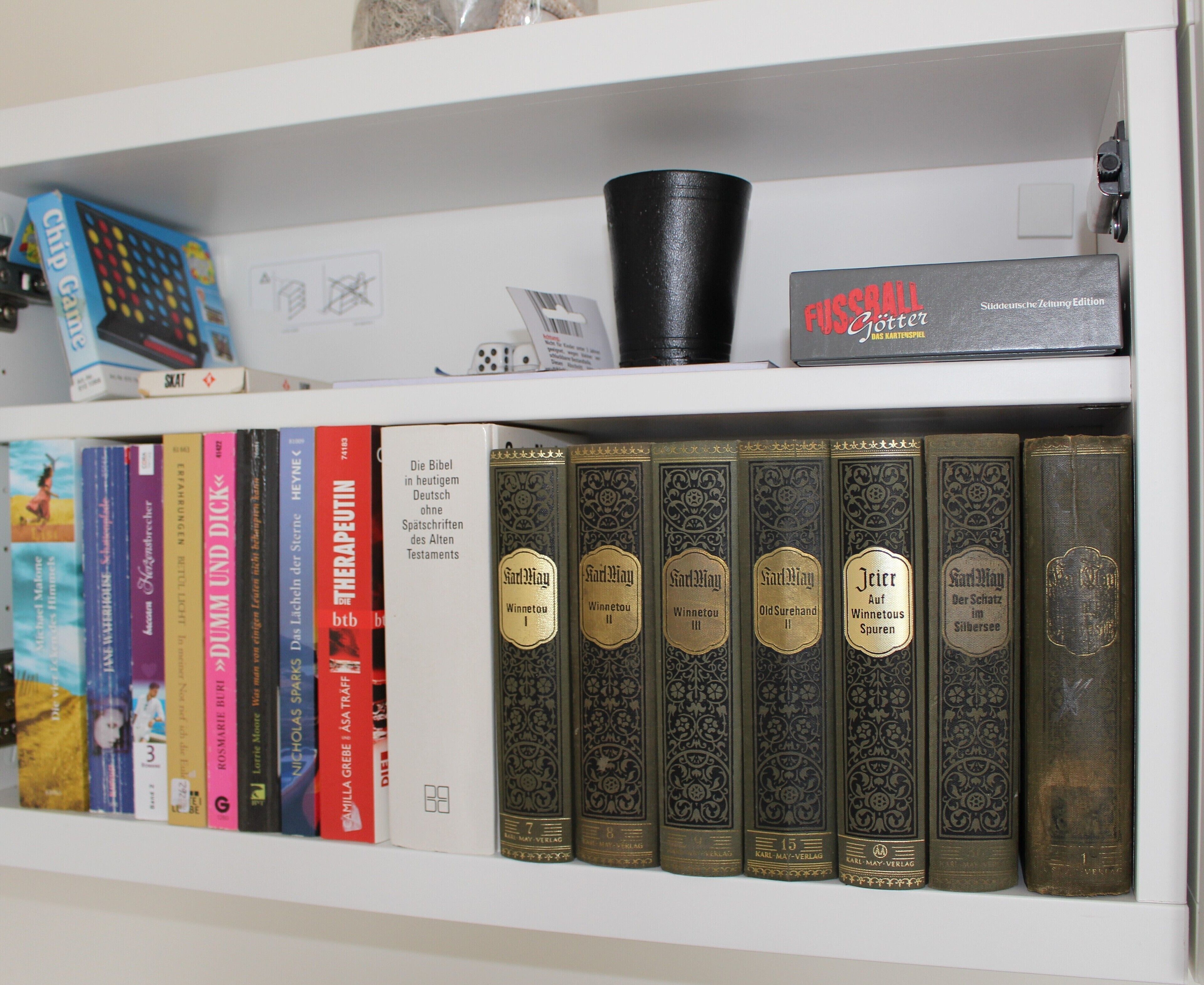 Une bibliothèque remplie de divers livres, dont certains ont des couvertures décorées, et une boîte étiquetée « FUSSCROLL ».