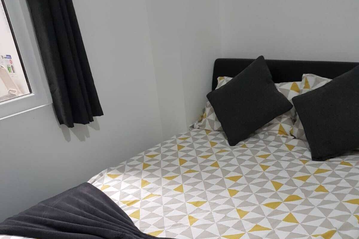 A neatly made bed with a geometric patterned bedspread, a dark throw blanket, and two pillows.
