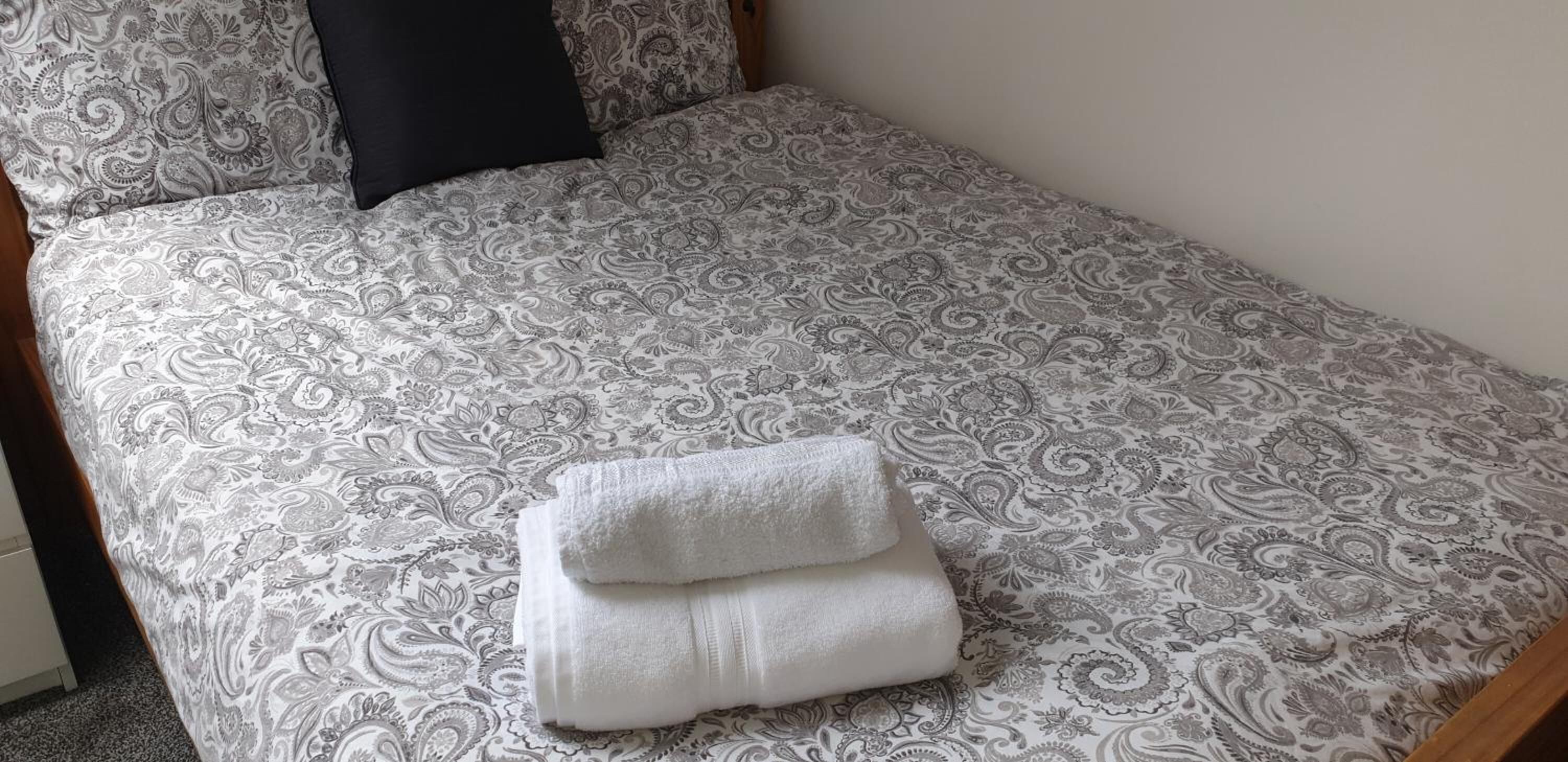 Una cama con un edredón estampado y dos toallas blancas dobladas con cuidado.