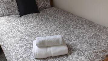 Una cama con un edredón estampado y dos toallas blancas dobladas con cuidado.