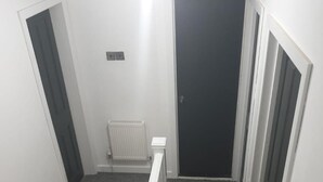Una escalera con peldaños alfombrados y barandillas blancas que conduce a una habitación con una puerta oscura y un radiador en la pared.