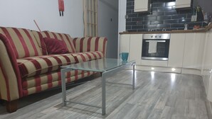 Una sala de estar con un sofá a rayas, una mesa de centro de vidrio y una cocina al fondo.