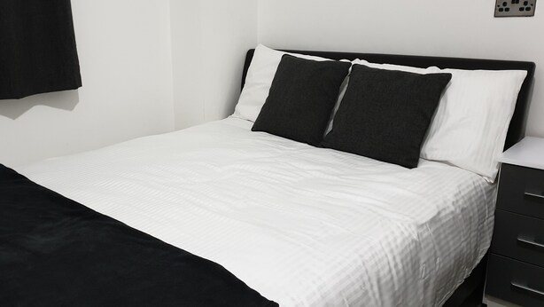 Una cama bien hecha con ropa de cama blanca y negra, una manta de color negro y un cabecero negro.