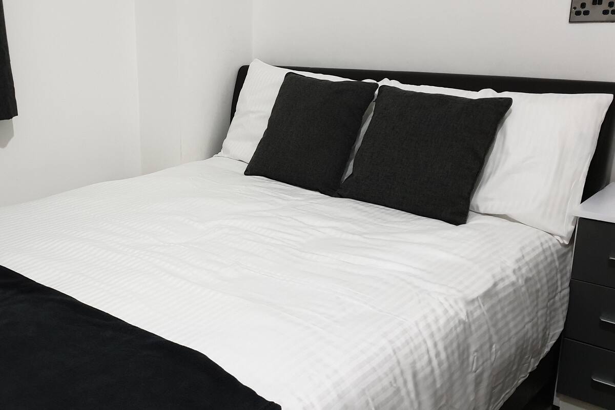 A neatly made bed with white and black bedding, a black throw blanket, and a black headboard.