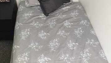 Una cama individual con una colcha gris estampada con flores y una almohada negra.