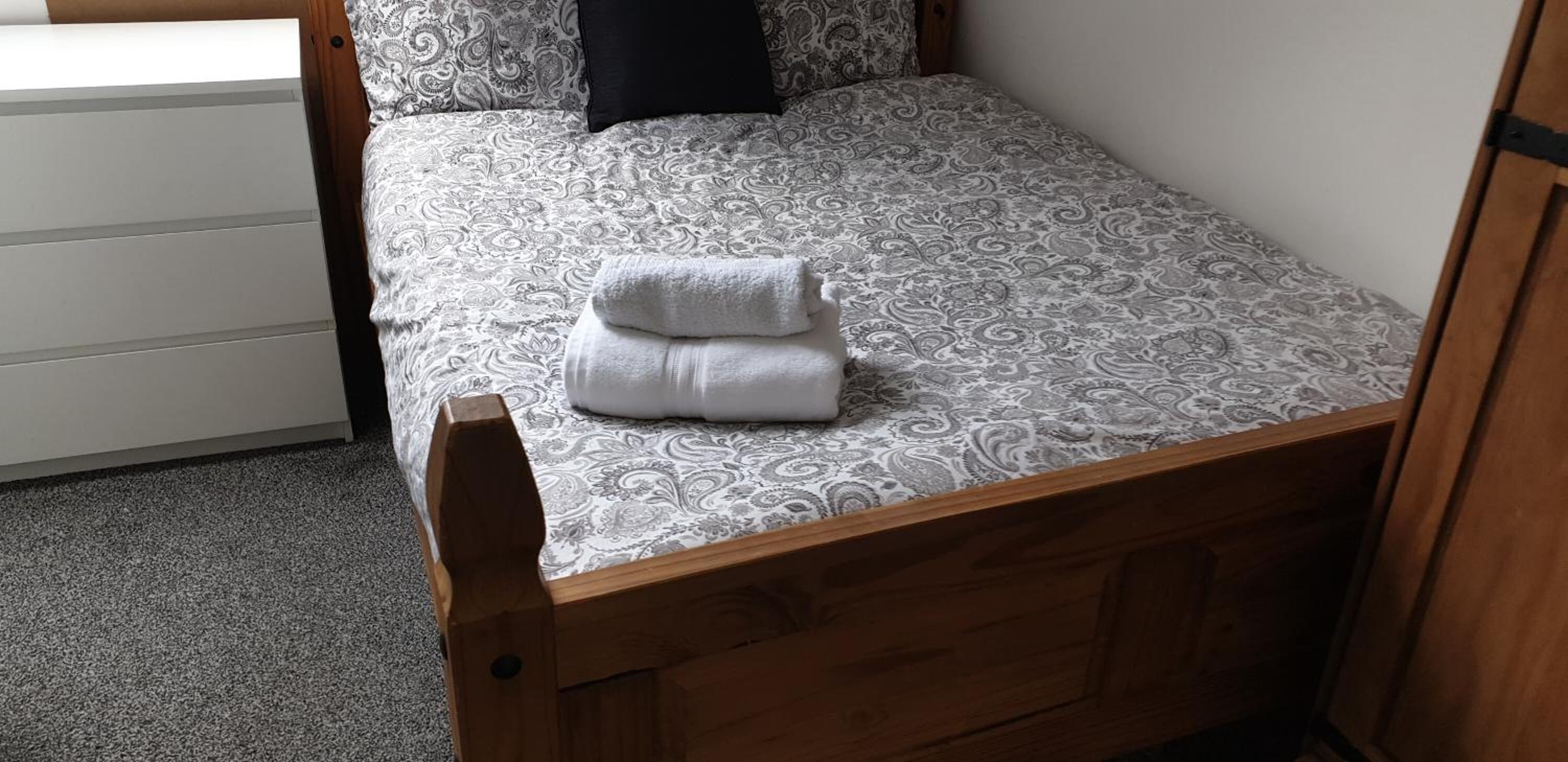 Una cama individual con una colcha estampada y una toalla blanca doblada cuidadosamente.