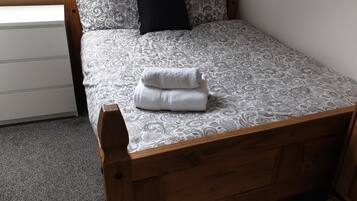 Una cama individual con una colcha estampada y una toalla blanca doblada cuidadosamente.