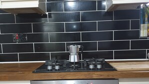 Una cocina con estufa a gas, horno y salpicadero de azulejos negros.