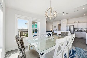 Een moderne keuken met witte kastjes, een roestvrijstalen koelkast en een eethoek met een glazen tafel en witte stoelen.