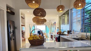 Une cuisine moderne dotée d’un îlot central, de trois tabourets en bois et de luminaires suspendus en osier.
