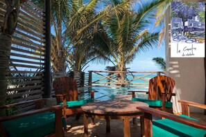 A wooden deck with chairs and a table overlooking a clear blue sea, with palm trees and a beach in the background. - La Casita de Chelem House / with a beautiful Mayan pool (Chelém)