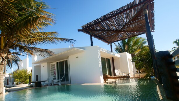 Un espace moderne aménagé au bord de la piscine, avec un bâtiment blanc, des chaises longues et des palmiers.