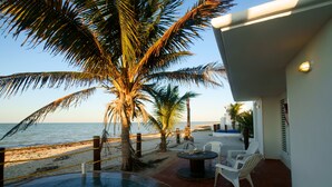 Un espace piscine offrant une vue sur la plage et l’océan, entouré de palmiers et de chaises blanches.