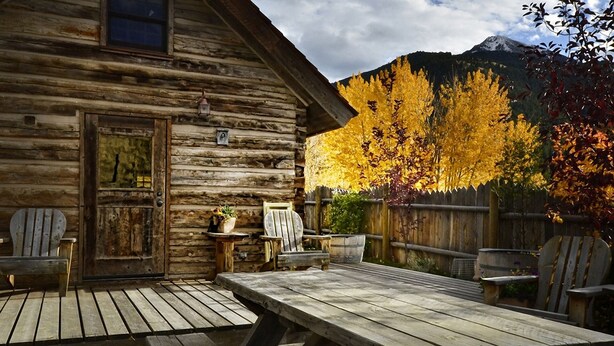A rustic wooden cabin with a covered patio, Adirondack chairs, and a table. - Cozy, Rustic Cabins near Chico Hot Springs & only 35 mins to YELLOWSTONE PARK!! (Pray)