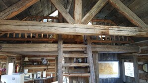 A rustic cabin interior with exposed wooden beams, a fireplace, and a window with a view. - Cozy, Rustic Cabins near Chico Hot Springs & only 35 mins to YELLOWSTONE PARK!! (Pray)