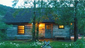 A rustic log cabin with a wooden door and windows, surrounded by trees and a grassy area. - Cozy, Rustic Cabins near Chico Hot Springs & only 35 mins to YELLOWSTONE PARK!! (Pray)