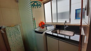 Une petite cuisine avec un évier, une fenêtre avec des stores et une serviette verte accrochée à un porte-serviettes.