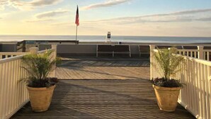 Um deck de madeira com duas plantas em vasos, uma bandeira e vista para o oceano.
